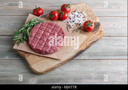 Die koteletts für Burger aus frischem Hackfleisch mit Gewürzen ende Kräutern auf einem Holztisch Stockfoto