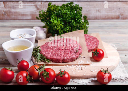 Die koteletts für Burger aus frischem Hackfleisch mit Gewürzen, Kräutern, Kirschtomaten auf einen hölzernen Tisch. Stockfoto