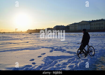 St. Petersburg, Russland - 07 März, 2018: ein Mann mit einem Fahrrad steht auf dem Eis der Fluss Newa und schaut den Sonnenuntergang in Sankt-Petersburg Stockfoto
