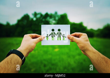 Man Hände halten ein weißes Blatt mit Silhouette Familie, Vater, Mutter und zwei Kinder. Familie Versicherung Konzept isoliert auf einem grünen Stockfoto