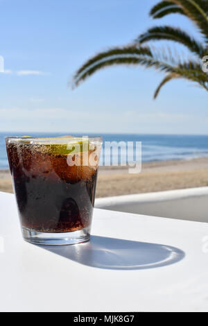 Ice Cola trinken am Strand mit Sand und Meer im Hintergrund auch eine große Palme, selektiver Fokus, auf einem weißen Vordergrund, Schuß für Kopie Raum Stockfoto