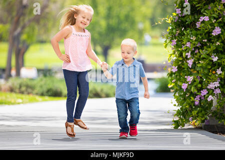 Junge Schwester und Bruder halten sich an den Händen und Laufen im Park. Stockfoto