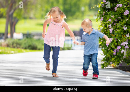 Junge Schwester und Bruder halten sich an den Händen und Laufen im Park. Stockfoto