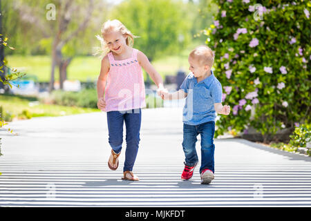 Junge Schwester und Bruder halten sich an den Händen und Laufen im Park. Stockfoto