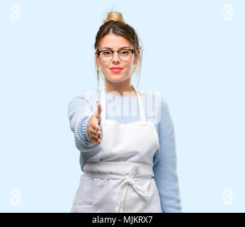 Junge Frau shop besitzer, tragen, Schürze hält Hände einladend im Handshake darstellen, Vertrauen und Erfolg Konzept, Begrüßung Stockfoto