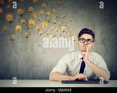 Junge nachdenklicher Mann in Gläsern am Tisch sitzen und denken über neue Ideen. Stockfoto