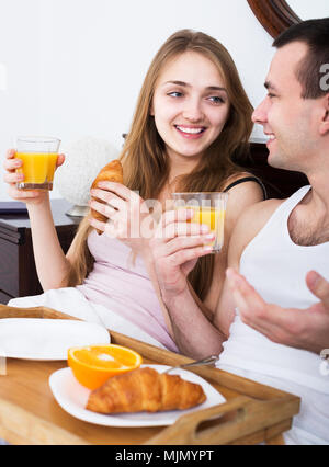 Junge Erwachsene mit orange Früchte und Saft zum Frühstück im Schlafzimmer Innenraum posing Stockfoto
