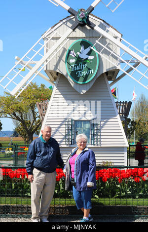 Gerne älteres Paar Lächeln beim Stehen vor der Windmühle bei Tulip Stadt warten auf das Foto aufgenommen zu werden. Tulip Stadt ist eine beliebte touristische Stockfoto
