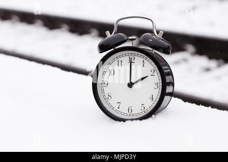 Eine schwarze Wecker auf Eisenbahnschienen draußen im Schnee. Stockfoto