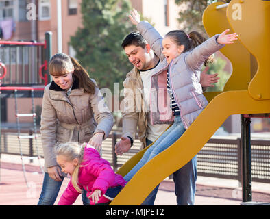 Freudige junge Eltern mit zwei aufgeregten kleinen Töchter Spaß an der Schiebetür board im Freien Stockfoto