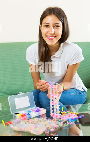 Lächelnde Frau macht braslets mit elastischen rainbow Webstuhl Bands Stockfoto