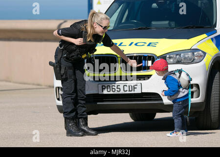 Toddler schaut auf Police Emergency blaues Licht mit bewaffneter weiblicher Polizeibeamtin in Blackpool, Großbritannien, Mai 2018. Urlauber am Blackpool Seafront. Tausende von Touristen und Urlaubern steigen am Strand von Blackpool an der Küste ab, um den schönen Sonnenschein und die hohen Temperaturen zu genießen. Stockfoto