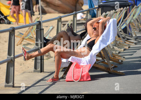 Boscombe, Bournemouth, Dorset, Großbritannien, 6.. Mai 2018, Wetter: Morgensonne an der Südküste an dem vielleicht heißesten Mayday-Feiertagswochenende auf Rekordzeit. Eine Frau, die in einem weißen Bikini auf einem Liegestuhl auf der Promenade entspannt und sonnenbaden geht. Stockfoto