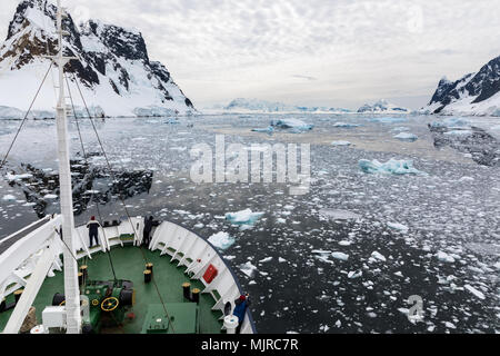 Ein Schiff fährt durch verschneite Berge und Wasser gefüllt mit Eis während Passagiere machen Sie Fotos und genießen Sie die Aussicht, Lemaire Kanal, Antarktis Stockfoto