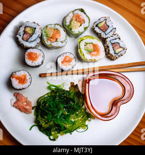 Hohe schräger Blick auf einen Teller mit Sushi und Stäbchen. Eine herzförmige glasigen Becher, mit Sojasauce. Stockfoto