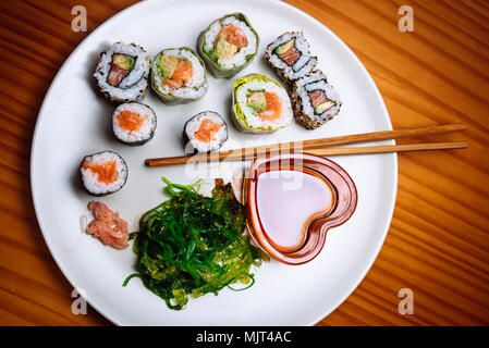 Hohe schräger Blick auf einen Teller mit Sushi und Stäbchen. Eine herzförmige glasigen Becher, mit Sojasauce. Stockfoto