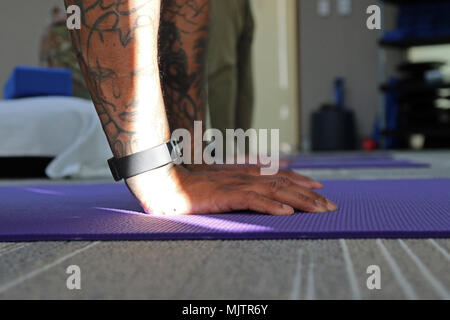 Ein Yoga Therapie Patienten bringt seine Hände auf die Matte an den unerschrockenen Geist in Fort Bragg, N.C., Dez. 14, 2017. Die Klinik konzentriert sich auf traumatische Verletzungen des Gehirns und die damit verbundenen Bedingungen und Yoga Therapie wird oft für Patienten empfohlen, die den Heilungsprozess zu erleichtern. Us-Armee Foto von Sgt. Paige Behringer) Stockfoto