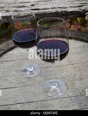 Zwei Gläser Rotwein saß oben auf der verwitterten Weinfass mit roten Herbst Weinlaub und Holzzaun Rail im Hintergrund Stockfoto