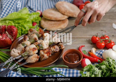 Die Hand, die geschmiedeten Gabel neigt, Kebabs, saftig. Fleisch über dem offenen Feuer gekocht. Rustikal. Still-life auf einem hölzernen Hintergrund. Close-up. Stockfoto