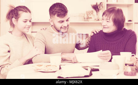 Freundliche ältere Frau mit erwachsenen Kindern zu arbeiten, ihre Finanzen zu Hause Analyse suchen Stockfoto