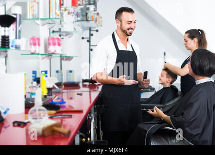 Mann Friseur im Gespräch mit Frau, die bereit ist, ihr Haar in überfüllten Beauty Salon zu schneiden Stockfoto