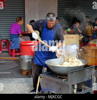 KAOHSIUNG, TAIWAN - 17. FEBRUAR 2018: ein Mann, der an einem Outdoor Essen kocht Stall gebratener Reis in einem großen Wok. Stockfoto