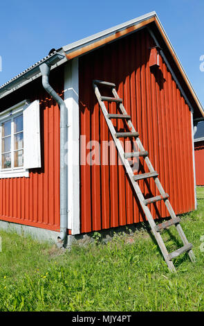 Eine Leiter an die Wand gelehnt auf einem rot lackierten kleinen Häuschen. Stockfoto