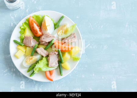 Nicoise Salat mit Thunfisch, Eier, Kartoffeln, grüne Bohnen und Tomaten. Traditionelle Nicoise Salat über blau Holz- Hintergrund, Ansicht von oben, kopieren. Stockfoto