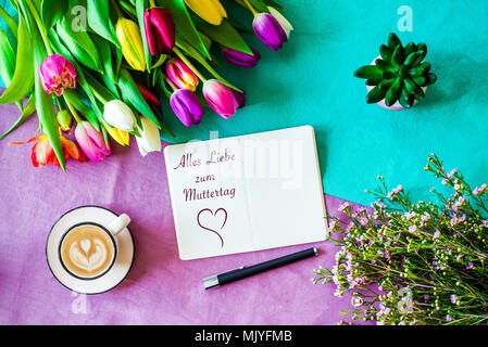 Von oben als flatlay mit der glücklichen Mutter Tag Nachricht in deutscher Sprache auf Notizen mit Kaffee und bunte Tulpen und Blumen geschrieben Schuß Stockfoto