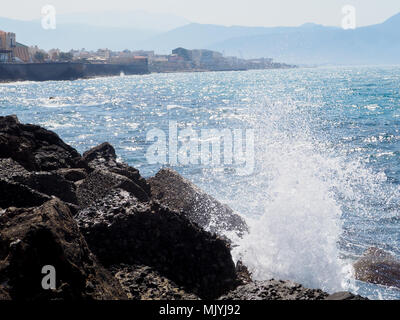 Spritzer aus den Wellen stoßen gegen die felsige Küste, das Meer ist blau Stockfoto