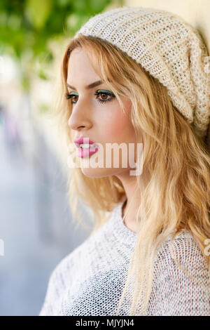 Close-up Profil der blonde junge Frau mit lockigem Haar. Mädchen mit Pullover und Wolle Gap im städtischen Hintergrund. Weibchen mit schönen Lippen in p lackiert Stockfoto