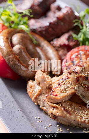 Verschiedene köstliche gegrillte Fleisch- und Wurstwaren mit Gemüse und Grüns. Stockfoto