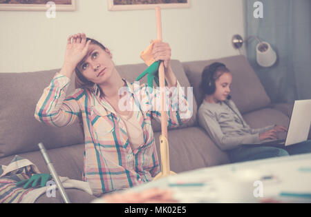 Müde Mutter sitzt in der Nähe des Tisches mit Mop nach der Reinigung home Stockfoto