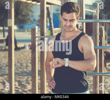 Körperlich fit Mann an smartwatch auf Sportplatz am Strand suchen Stockfoto