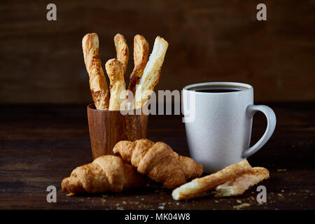 Weißes Porzellan Tasse Kaffee, Croissants und frisch gebackene Grissini auf einem alten Holz- Hintergrund, Nahaufnahme, selektiven Fokus. Köstliches Gebäck auf Tropfen, Stockfoto