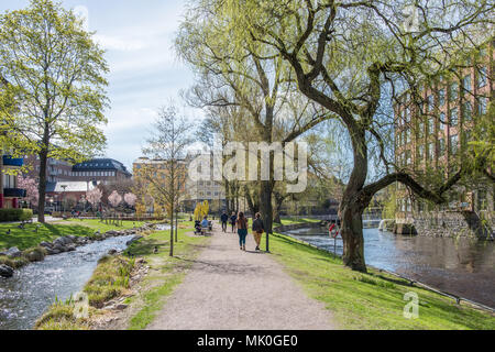 Nicht erkennbare Menschen gehen in Waterfront Park Strömparken entlang Fluss Motala in Norrköping im Frühjahr in Schweden Stockfoto