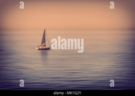 Lonely Segelboot in der Mitte des ruhigen Meer bei Sonnenuntergang Stockfoto