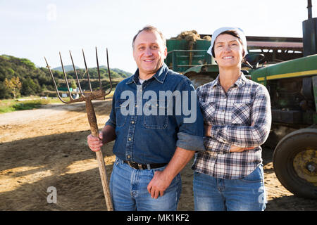 Zuversichtlich älterer Mann und Frau Besitzer der Farm in der Nähe von Traktor im Freien Stockfoto