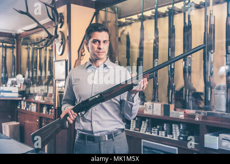 Brunette männlichen Jäger Wahl Schrotflinte in Store mit Hunt Ausrüstung Stockfoto