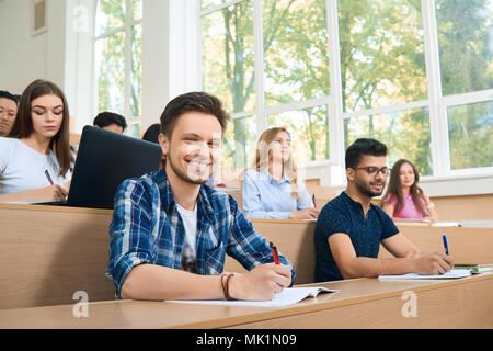 Vorderansicht des studuing während der Lektion Studenten. Groupmates konzentrieren sich auf die Arbeit. Mit Laptops und Smartphones. Modenr sitzen im Klassenzimmer mit grossen spacig, Panoramafenster. Stockfoto