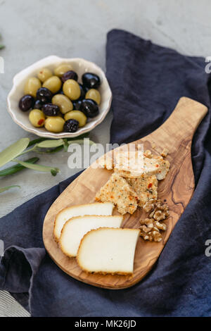 Kleines Käsebrett mit zwei verschiedenen Sorten Käse auf schwarz Bettwäsche und Oliven in Muschel geformten Keramikplatte. Vertikale Komposition. Stockfoto