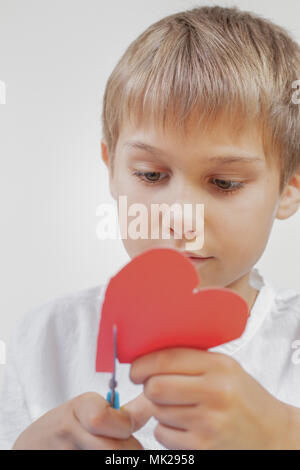 Kind schneiden Rotes Herz aus Papier mit einer Schere Stockfoto