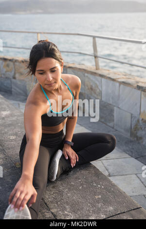 Eine sportliche Frau die Ausübung von der Strandpromenade, erstreckt sich in schwarzen Strumpfhosen und grau Tank Top Stockfoto