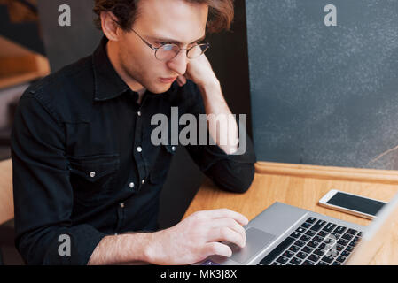 Kreative Menschen Designer arbeiten auf seinem Laptop Computer, während für Aufträge, die an seinem Lieblingscafé drinnen warten, männliche Kursteilnehmer auf Net Working - buchen Sie beim morgendlichen Frühstück in modernen Kaffee Shop Interior Stockfoto