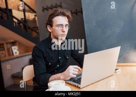 Kreative Menschen Designer arbeiten auf seinem Laptop Computer, während für Aufträge, die an seinem Lieblingscafé drinnen warten, männliche Kursteilnehmer auf Net Working - buchen Sie beim morgendlichen Frühstück in modernen Kaffee Shop Interior Stockfoto