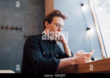 Soft Focus. Mann hält und mit Phone verkaufen. beim Sitzen und auf dem Sofa im modernen Haus entspannen. Konzept für junge Menschen, die mobiles Gerät Stockfoto