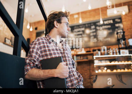 Begabte junge Mann in casual Shirt Zeichnung Skizze in Notebook genießen Freizeit im Coffee Shop. Qualifizierte Studenten schreiben Hausaufgaben in Notepad sitzen in Coworking Stockfoto