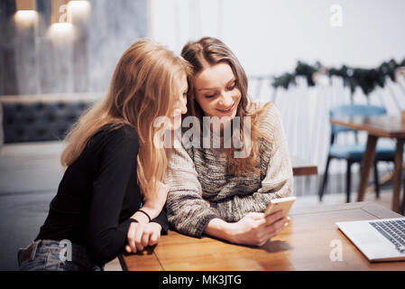 One-on-one Meeting. Zwei junge business Frauen am Tisch sitzen im Cafe. Mädchen zeigt ihrer Freundin Bild auf dem Bildschirm des Smartphones. Am Tisch ist Notebook geschlossen. Freunde treffen Stockfoto