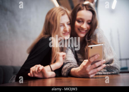 One-on-one Meeting. Zwei junge business Frauen am Tisch sitzen im Cafe. Mädchen zeigt ihrer Freundin Bild auf dem Bildschirm des Smartphones. Am Tisch ist Notebook geschlossen. Freunde treffen Stockfoto