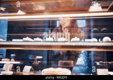 Lächelnde Frau an der Kamera über den Showcase mit süßen und Kuchen in der modernen Cafe innen Stockfoto